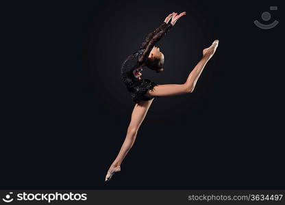 Young cute woman in gymnast suit show athletic skill on black background