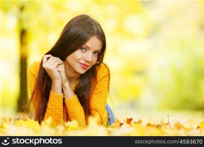 Young cute woman laying on dry leaves in autumn park