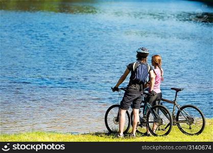 Young cyclist couple standing and watching the lake
