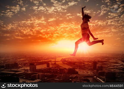 Young dancer. Silhouette of dancer jumping against city in lights of sunrise