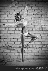 Young dancing woman on grey brick wall background (monochrome version)