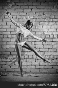 Young dancing woman on grey brick wall background (monochrome version)