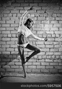Young dancing woman on grey brick wall background (monochrome version)