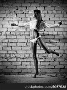 Young dancing woman on grey brick wall background (monochrome version)