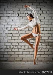 Young dancing woman on grey brick wall background (normal version)