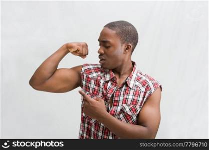 Young dark skinned handsome guy proudly pointing at his biceps showing how strong he is wearing a checkered shirt, isaolated
