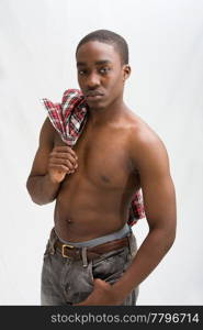 Young dark skinned handsome guy standing like a macho with a hand hanging from his pocket and the other holding a checkered shirt over his shoulder and showing his six pack, isolated.