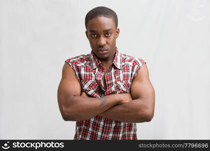 Young dark skinned handsome guy standing like a macho with both arms crossed wearing a checkerd shirt without sleeves.