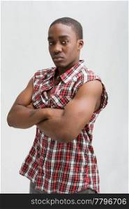 Young dark skinned handsome guy standing like a macho with both arms crossed wearing a checkerd shirt without sleeves.