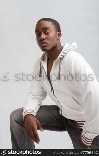 Young dark skinned handsome guy standing like a macho with one leg up and leaning on it with one arm, isolated