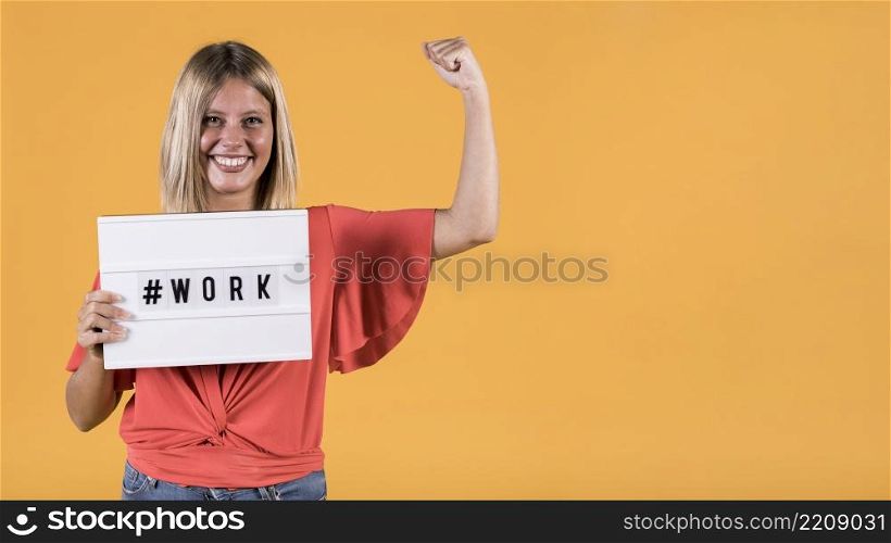 young deaf woman holding light box with hash tag work text flexing muscle yellow backdrop