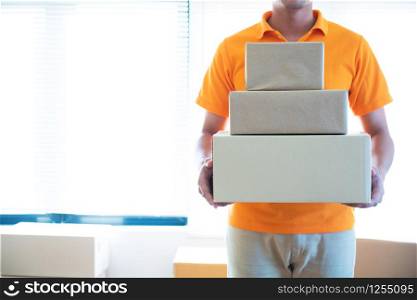 Young delivery asian man in uniform holding and carrying stack of cardboard postel in office.