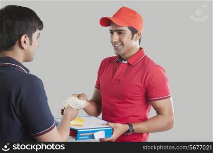 Young delivery man delivering pizza to customer over gray background