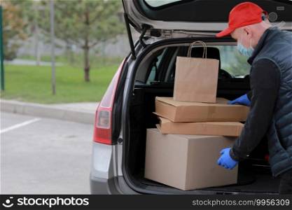 Young delivery man in protective mask, red cap and gloves near the car with boxes and packages, outdoors. Service coronavirus. Online shopping. mock up. Young delivery man in protective mask, red cap and gloves near the car with boxes and packages, outdoors. Service coronavirus. Online shopping. mock up.