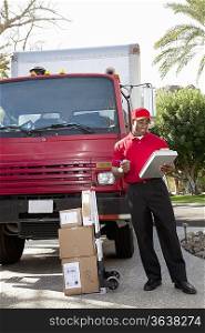 Young delivery man looking at delivery list on clipboard with truck in background