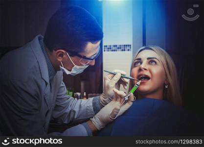 Young dentist treating woman in the office in blue lighting. Woman seeing a dentist