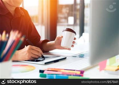 Young designer sitting at desktop computer having some hot coffee in morning