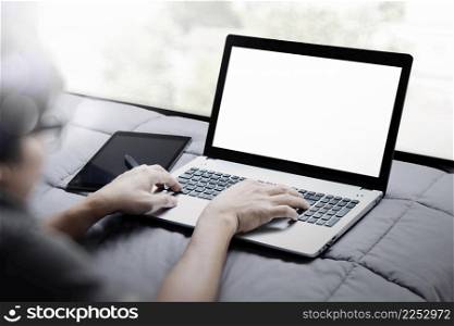 young designer working with smart phone and blank screen laptop computer in bed as concept