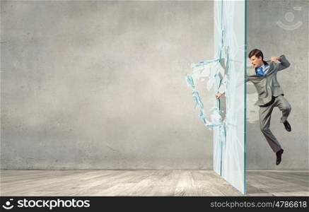 Young determined businessman breaking glass with karate punch. Businessman in anger