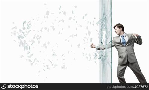 Young determined businessman breaking glass with karate punch. Businessman in anger