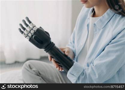 Young disabled girl customizing her sensory prosthetic arm, close-up. Female with disability using robotic prosthesis after limb loss. Application of bionic hands. Medical technologies.. Application of bionic hands. Disabled woman customizing sensory robotic prosthetic arm, close up