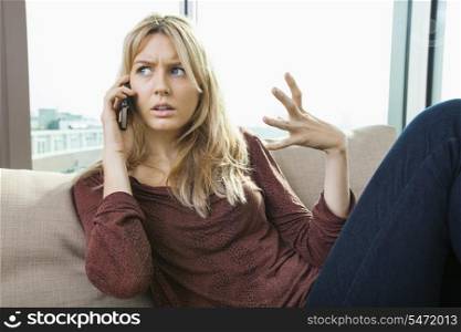 Young displeased woman talking on mobile phone at home