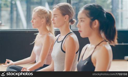 Young diversity sporty people practicing yoga lesson with instructor. Multi racial group of women exercising healthy lifestyle in fitness studio. Sport activity, gymnastics or ballet dancing class.