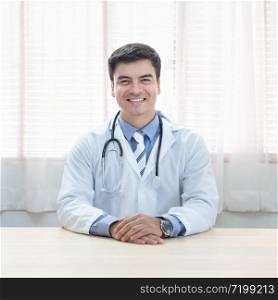 Young doctor caucasian man sitting at the desk at his working place and smiling looking at camera. Perfect medical service in clinic. Happy future of medicine and healthcare.