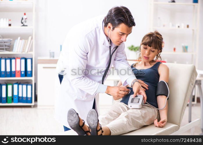 Young doctor checking pregnant woman’s blood pressure