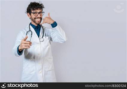 Young doctor making call gesture isolated. Smiling doctor making call gesture and pointing at the camera.