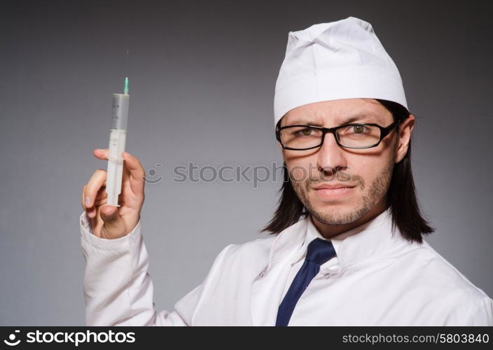 Young doctor man with syringe against grey background