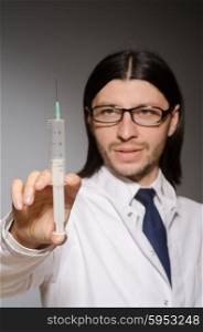 Young doctor man with syringe against grey background