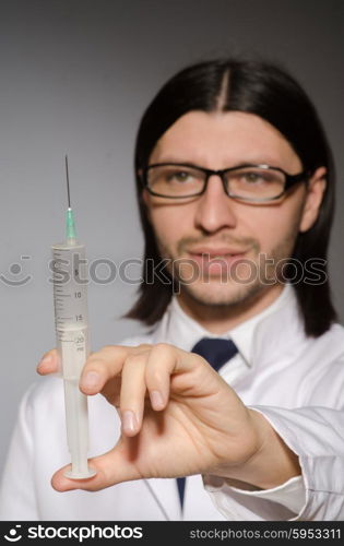 Young doctor man with syringe against grey background