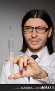 Young doctor man with syringe against grey background