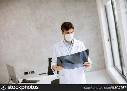 Young doctor with protective facial mask examining xray in the office