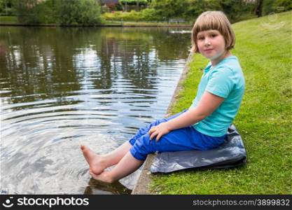Young dutch girl sitting with feet in water of pond in park
