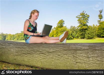 Young dutch woman sits on tree trunk in nature working on laptop