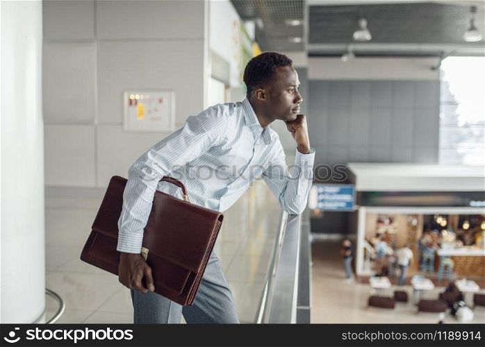Young ebony businessman with briefcase looking on food-court. Successful business person in cafe, black man in formal wear