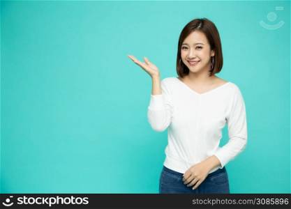Young elegant Asian woman smiling and presenting to empty copy space isolated on green background, Thai model