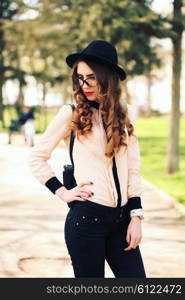 Young elegant woman in stylish clothes. Model with red lips in hipster cloth and vintage black hat in sunglasses. Fashion shot. Modern youth lifestyle concept.