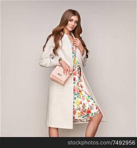 Young elegant woman in trendy white coat. Blond hair, floral dress, isolated studio shot. Fashion autumn lookbook. Model woman with handbag