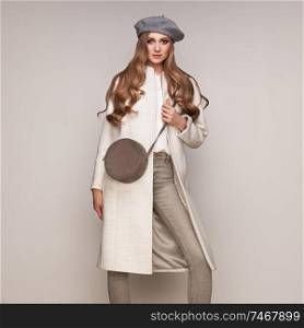 Young elegant woman in trendy white coat. Blond hair, gray beret, isolated studio shot. Fashion autumn lookbook. Model woman with handbag