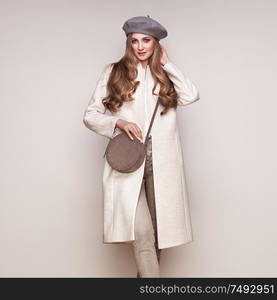 Young elegant woman in trendy white coat. Blond hair, gray beret, isolated studio shot. Fashion autumn lookbook. Model woman with handbag