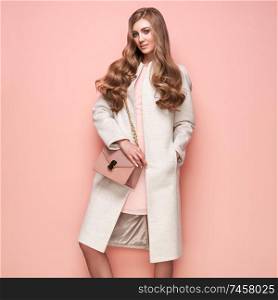 Young elegant woman in trendy white coat. Blond hair, pink dress, isolated studio shot. Fashion autumn lookbook. Model woman with handbag