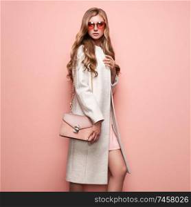 Young elegant woman in trendy white coat. Blond hair, pink dress, isolated studio shot. Fashion autumn lookbook. Model woman with handbag