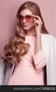 Young elegant woman in trendy white coat. Blond hair, pink dress, isolated studio shot. Fashion autumn lookbook. Model woman in sunglasses