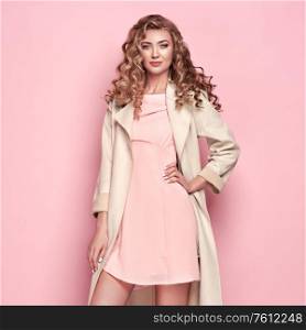 Young elegant woman in trendy white coat. Blonde hair, coral dress, isolated on pink background, studio shot. Fashion spring lookbook