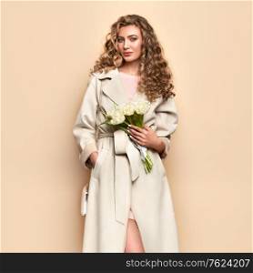 Young elegant woman in trendy white coat. Blonde hair, coral dress, isolated on beige background, studio shot. Fashion spring lookbook. Model woman with handbag