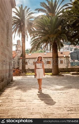 Young elegant woman walking on street with ancient building and high palms