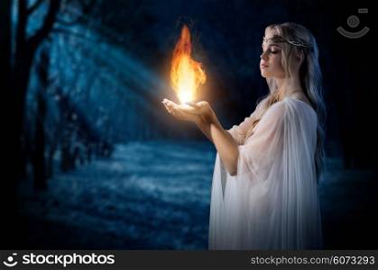 Young elven girl holding fire in palms at night forest